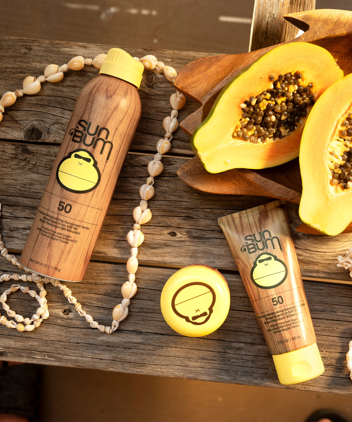 Sun Bum sunscreen bottles and a halved papaya on a wooden surface