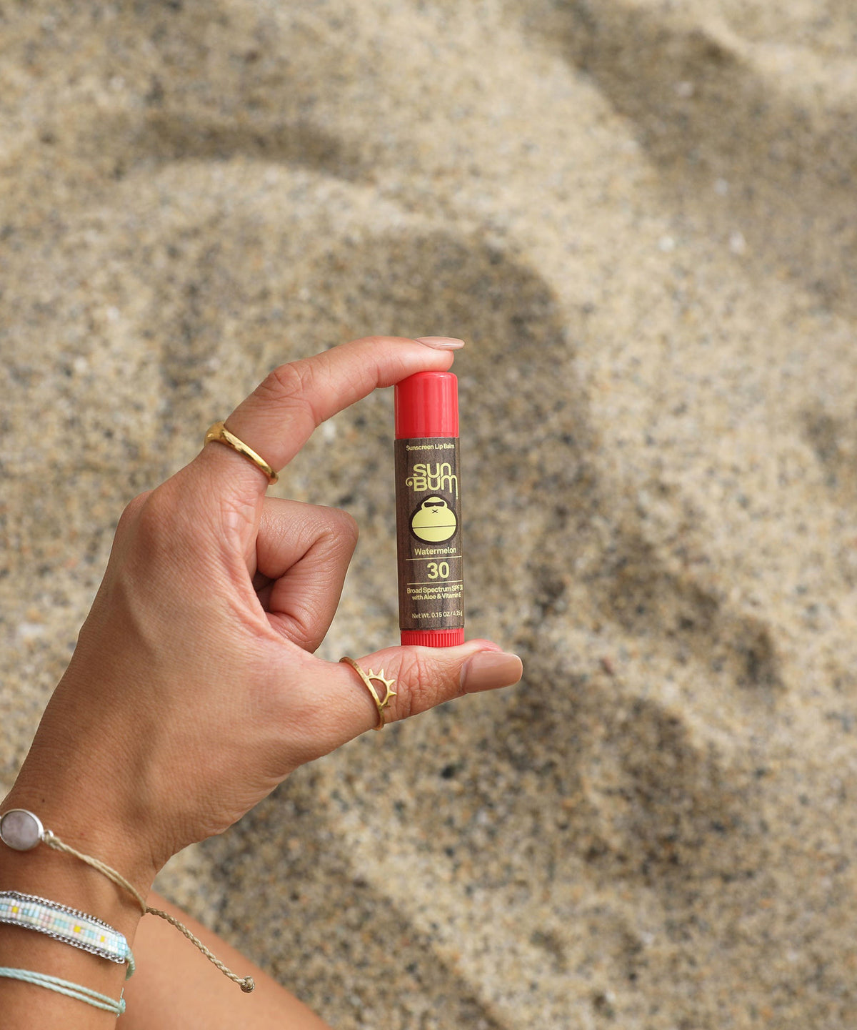 Hand holding a Sun Bum sunscreen stick on a sandy background
